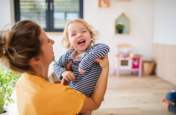 Alegre joven madre con hija pequeña en el interior en el dormitorio jugando . — Foto de Stock