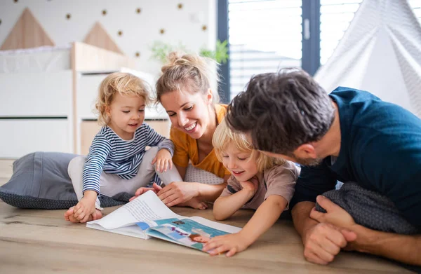 Ung familie med to små barn innendørs på soverommet som leser en bok . – stockfoto