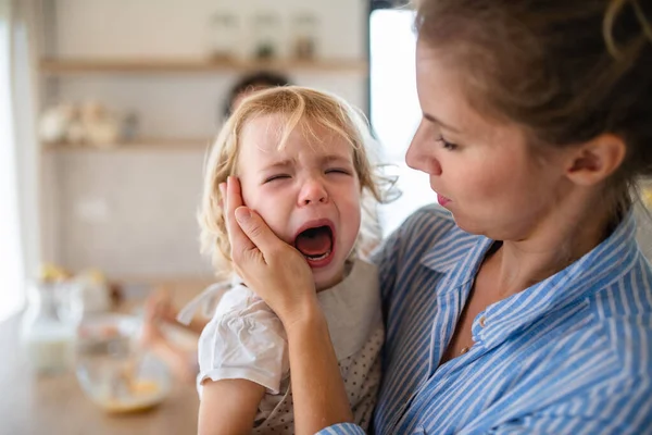 Eine Mutter hält eine weinende Kleinkind-Tochter in der Küche. — Stockfoto