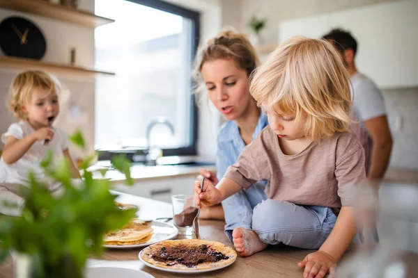 Família jovem com duas crianças pequenas dentro de casa na cozinha, comendo panquecas . — Fotografia de Stock