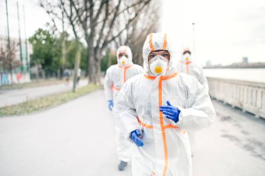 Koruyucu giysileri ve solunum cihazları olan insanlar dışarıda koşuyor, koronavirüs konsepti..