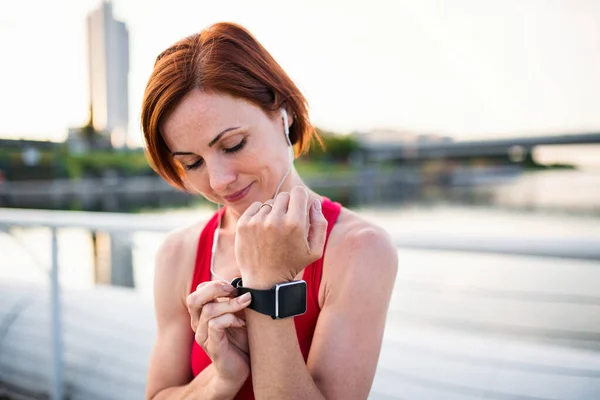 Jovem corredor com fones de ouvido na cidade, usando smartwatch . — Fotografia de Stock