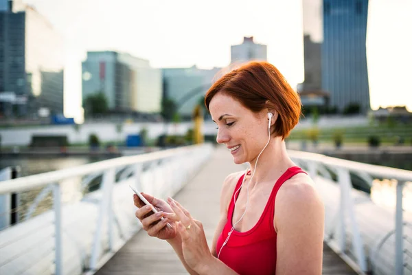 Giovane donna corridore con auricolari in città, utilizzando smartphone . — Foto Stock