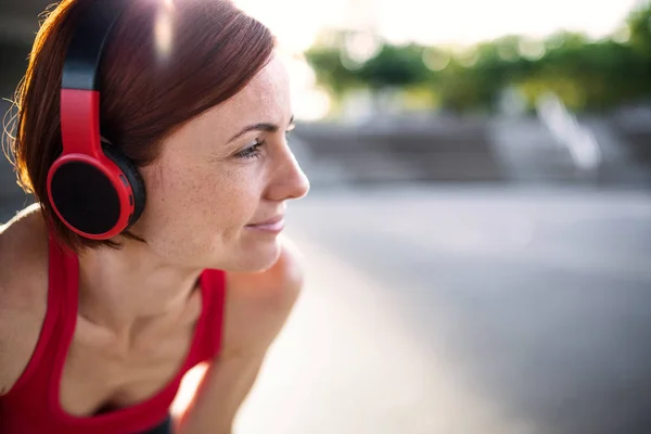 Young woman with headphones resting after doing exercise outdoors in city. — Stock Photo, Image