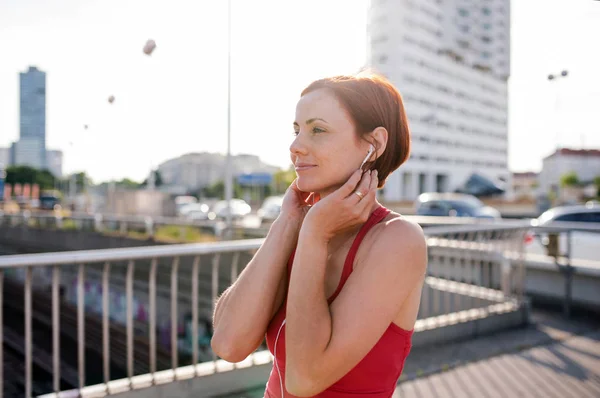 Een jonge vrouw runner met oortjes in de stad, rusten. — Stockfoto