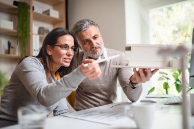 Modeli ev olan mimarlar ofisteki masa başında oturuyor, çalışıyor..