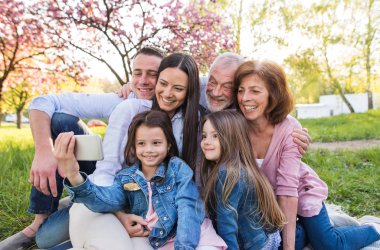 Three generation family sitting outside in spring nature, taking selfie. clipart