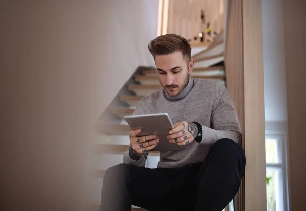 Jeune homme assis sur les escaliers à l'intérieur dans le bureau, en utilisant une tablette . — Photo