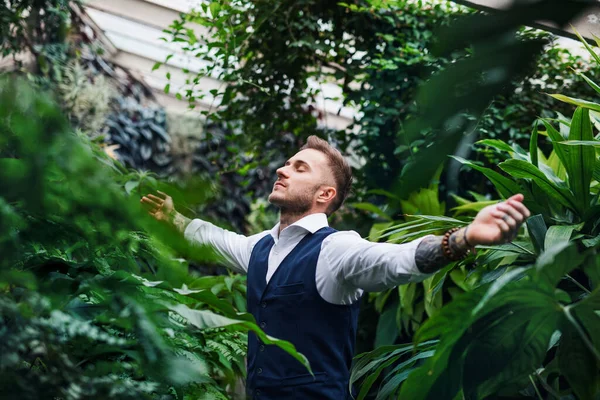 Young man standing in botanical garden, arms stretched. — Stock Photo, Image