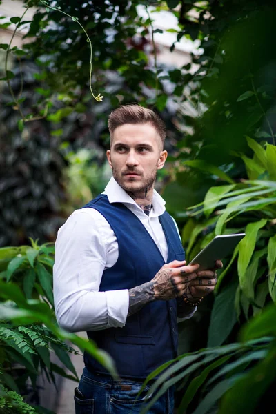 Młody człowiek z tabletem stojący w ogrodzie botanicznym. — Zdjęcie stockowe