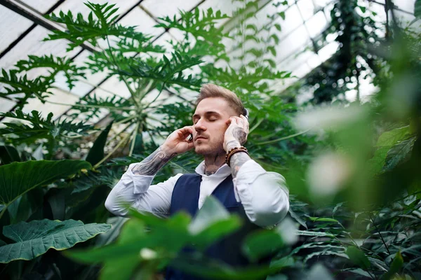 Молодой человек в наушниках стоит в ботаническом саду . — стоковое фото