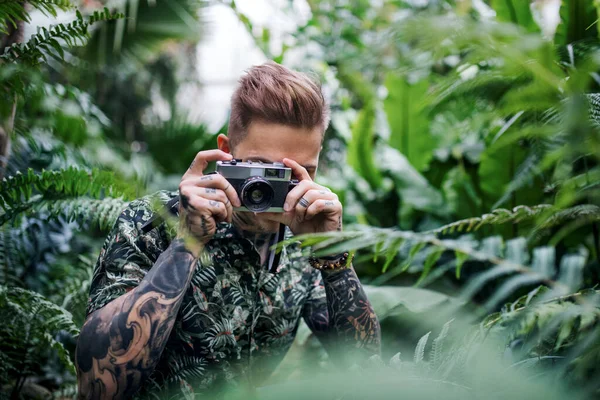 Młody człowiek z kamerą stojący w ogrodzie botanicznym, robiący zdjęcia. — Zdjęcie stockowe