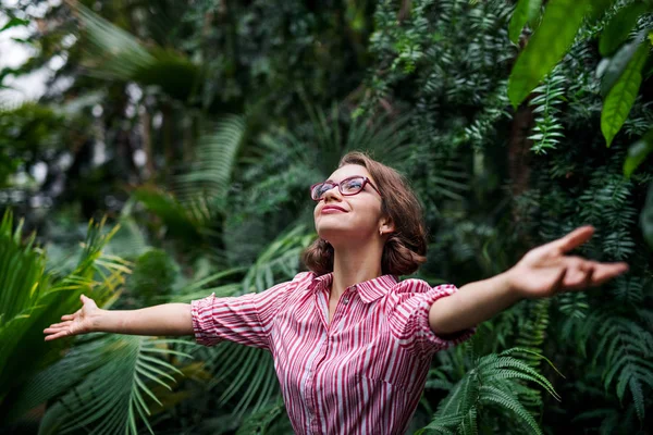 年轻的女人站在植物园里，张开双臂. — 图库照片