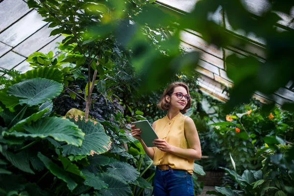 Mujer joven con tableta de pie en el jardín botánico. Copiar espacio . — Foto de Stock