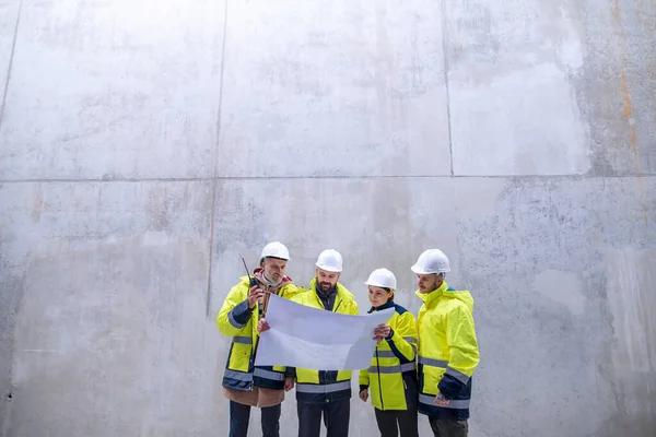 Um grupo de engenheiros de pé contra a parede de concreto no canteiro de obras . — Fotografia de Stock