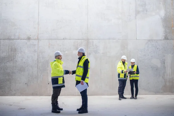 Un gruppo di ingegneri in piedi sul cantiere, stringendo la mano . — Foto Stock