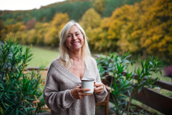 Senior woman with coffee standing outdoors on terrace, looking at camera. — Stock Photo, Image