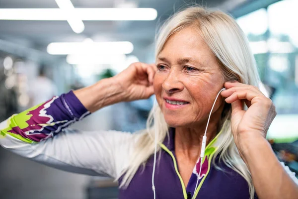 En äldre kvinna med hörlurar i gymmet vilar efter att ha gjort motion. — Stockfoto