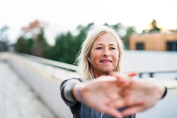 Een oudere vrouw met een koptelefoon buiten aan het sporten. — Stockfoto