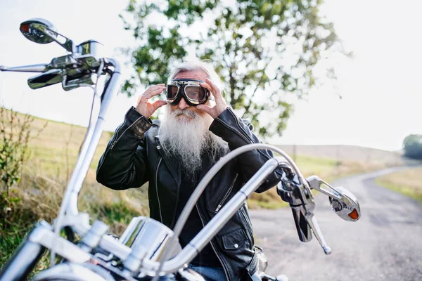 Ein älterer Mann mit Motorrad und Schutzbrille auf dem Land. — Stockfoto