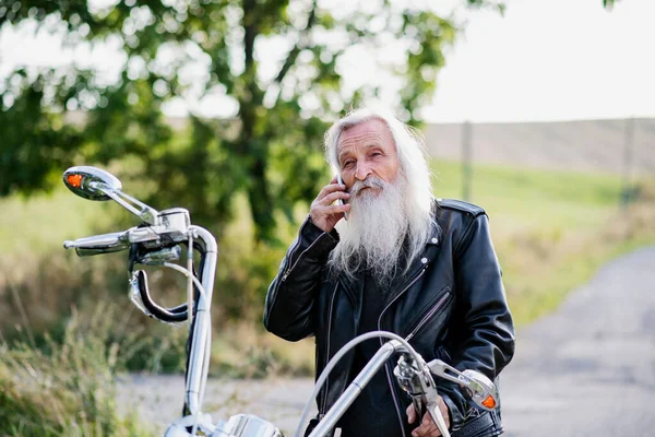 Hombre mayor viajero con moto en el campo, utilizando el teléfono inteligente . — Foto de Stock