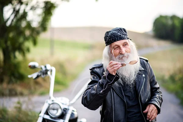 Senior man traveller with motorbike and sunglasses in countryside. — Stock Photo, Image