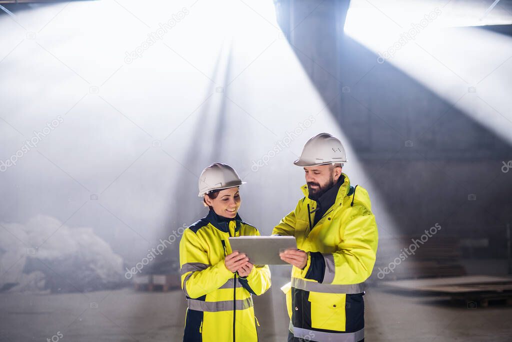 Engineers standing outdoors on construction site, holding tablet.