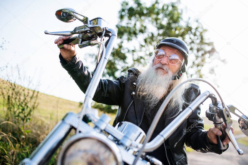 A senior man traveller with motorbike and sunglasses in countryside.