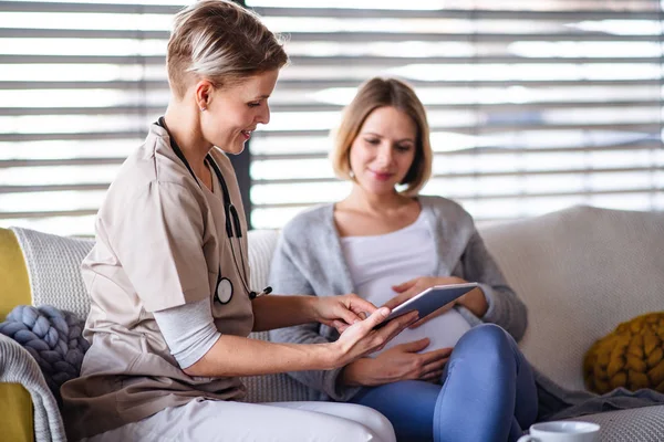 Een zorgverlener met tablet die thuis met een zwangere vrouw praat. — Stockfoto