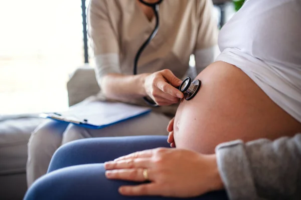 Une section médiane du travailleur de la santé examinant la femme enceinte à l'intérieur à la maison . — Photo