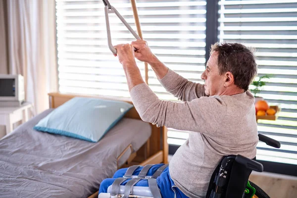 Man senior patient in wheelchair in hospital, holding onto a bed hanger. — Stock Photo, Image