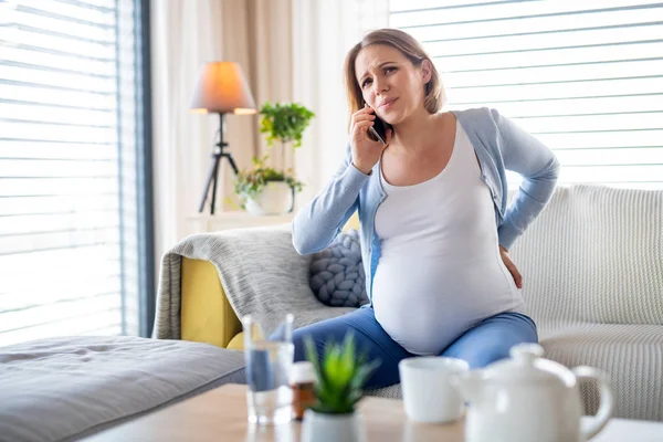 Portret van een zwangere vrouw die thuis pijn heeft, die thuis telefoneert. — Stockfoto