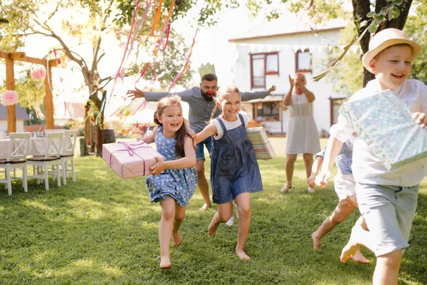 Small children ruunning with present outdoors in garden on birthday party. — Stock Photo, Image