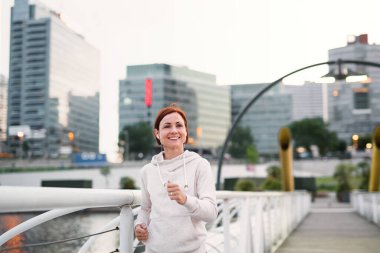 Şehirde koşu kulaklıklı genç kadın koşucunun ön görünümü.