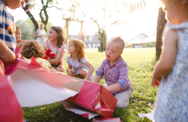 Синдром Дауна дитина з друзями на день народження на відкритому повітрі, відкриття подарунків . — стокове фото