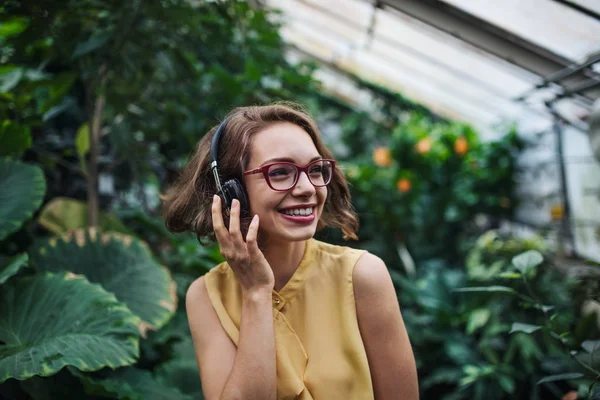 Botanik bahçesindeki serada duran kulaklıklı genç bir kadın.. — Stok fotoğraf