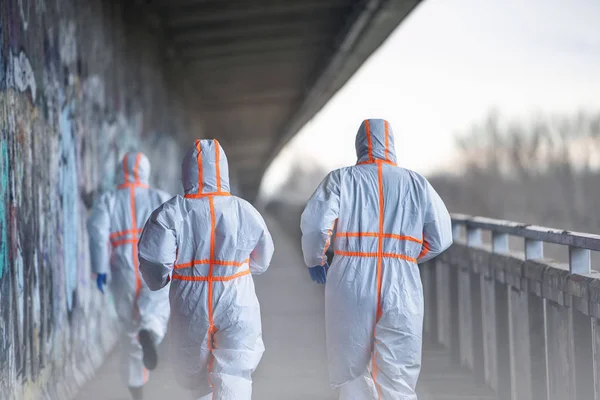 Rückansicht von Menschen mit Schutzanzügen, die im Freien laufen, Coronavirus-Konzept. — Stockfoto