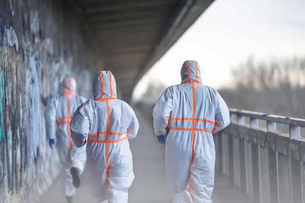 Vista posteriore delle persone con tute protettive che corrono all'aperto, concetto di coronavirus . — Foto Stock