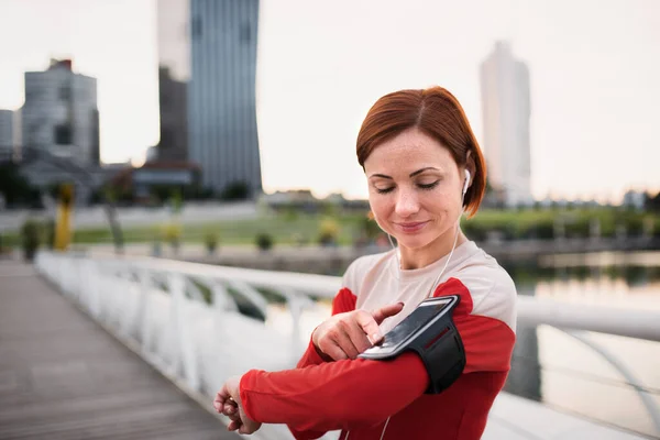 Corredor de mujer joven con auriculares en la ciudad, usando teléfono inteligente . —  Fotos de Stock