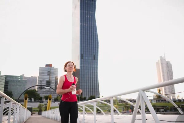 Vista frontale di giovane donna corridore con auricolari che fanno jogging in città . — Foto Stock