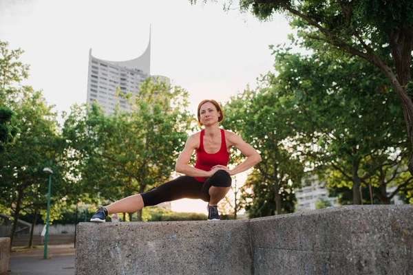 Mujer joven haciendo ejercicio al aire libre en la ciudad al atardecer, estirándose . — Foto de Stock