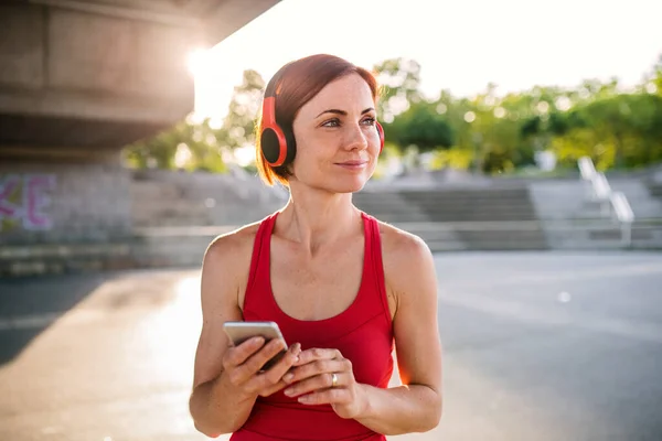 Young woman runner with headphones in city, using smartphone. — Stock Photo, Image