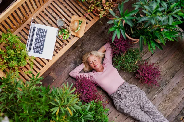 Vista superior de la mujer mayor con el ordenador portátil que miente al aire libre en la terraza, descansando . — Foto de Stock