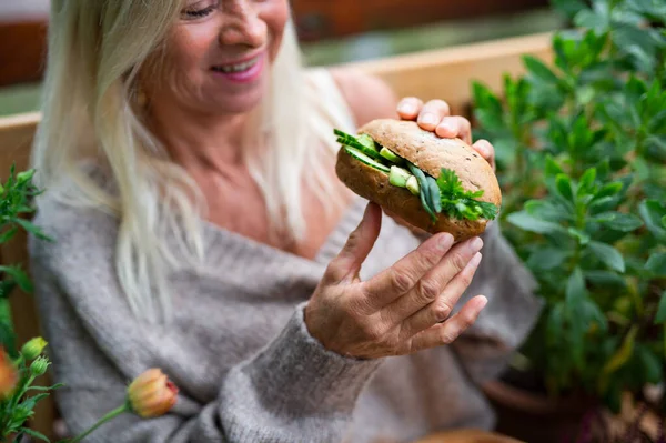 Starší žena venku na terase, jí zeleninový sendvič. — Stock fotografie