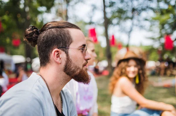 Boční pohled na mladého muže sedícího na letním festivalu. — Stock fotografie