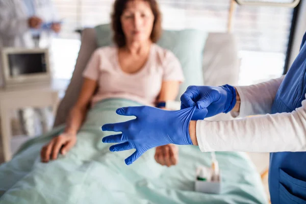 Onherkenbare arts met patiënt in bed in het ziekenhuis, handschoenen aandoen. — Stockfoto