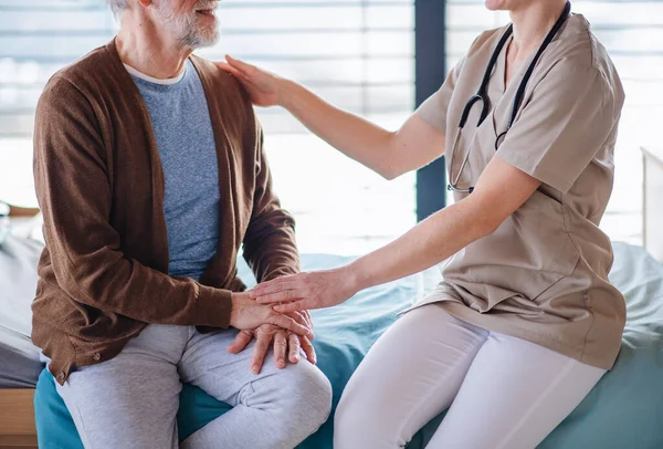 En kvinnlig läkare talar med äldre patienter i sängen på sjukhus, mittsektionen. — Stockfoto