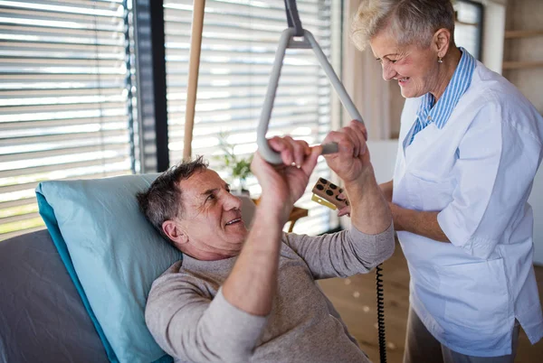 Pracownik służby zdrowia pomaga sparaliżowanemu starszemu pacjentowi w szpitalu. — Zdjęcie stockowe