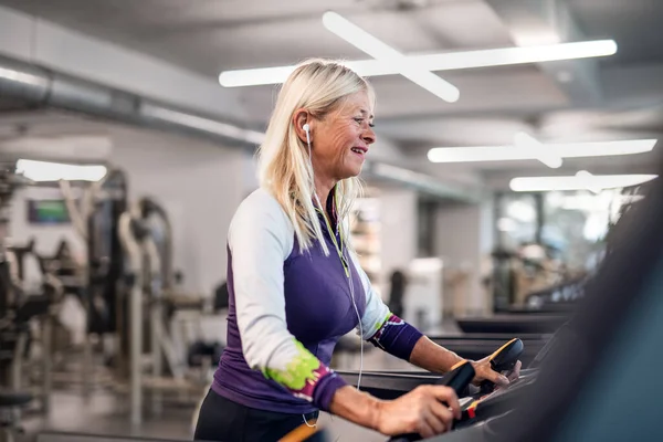 En äldre kvinna med hörlurar på gymmet tränar konditionsträning. — Stockfoto