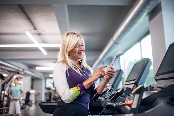 Eine Seniorin mit Smartphone im Fitnessstudio beim Ausdauertraining. — Stockfoto